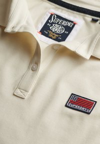 Crème polo shirt van gestructureerde stof, met een drieknoopsluiting. Opvallende Superdry-logo patch met een vlagontwerp op de linkerborst.