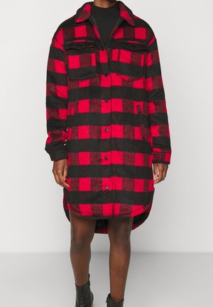 Persona que lleva un abrigo largo de cuadros rojos y negros con botones, dos bolsillos en el pecho y botines negros.