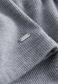Tessuto lavorato a maglia grigio con una texture a coste, con un'etichetta metallica embossata con la scritta "DOWNTIME" attaccata al materiale.