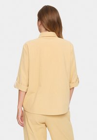 Yellow, short-sleeve shirt with a collar, rolled cuffs, and a casual fit. Fabric has a textured finish and smooth appearance.