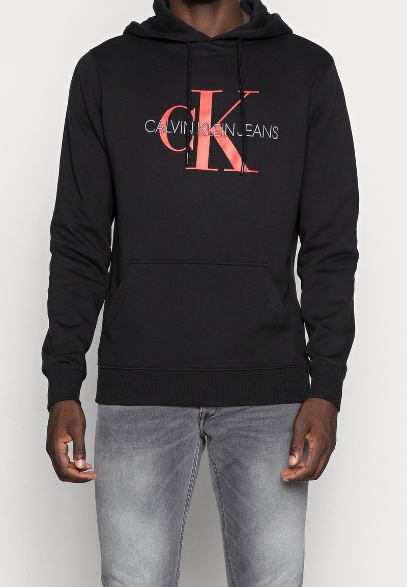 Sudadera negra hecha de una mezcla de algodón, con un estampado del logotipo de Calvin Klein en rojo y blanco en la parte frontal, con un bolsillo canguro y capucha con cuerda.