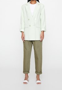 Lysegrøn dobbeltradet blazer i blødt stof med to knapper og opkørte ærmer, kombineret med olivengrønne bukser med opkrogede ben og hvide sandaler.