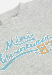 Felpa in cotone grigia caratterizzata da un collo tondo a coste. La grafica frontale presenta un testo blu e arancione con la scritta "Mini Avventuriero 83."