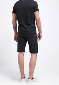 Svart bomull t-shirt och svarta denimshorts, som visar en slät textur. Vita sneakers fulländar outfiten med en enkel, odekorerad design.