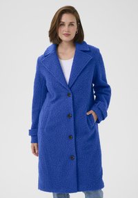 Cabană albastră din fleece cu un finisaj texturat, guler mare, închidere cu buton și buzunare laterale, stilizată pentru o croială lejera.