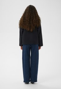 Schwarzer übergroßer Pullover und weite dunkelblaue Jeans mit glatter Textur und lockerem Sitz, von hinten vor einem schlichten Hintergrund gesehen.