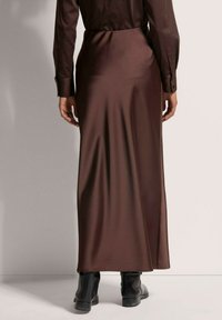 Bruine satijnen maxi rok met een gladde textuur, met een strakke taille en vloeiende silhouet, gecombineerd met zwarte enkellaarsjes.