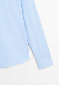 Manche de chemise bleu clair avec fines rayures blanches verticales et poignet à un bouton sur fond blanc.