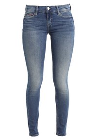Jeans ajustados en denim azul medio con parches desgastados, cinco bolsillos, cremallera y cierre de botón de metal. Detalle de costura sutil.