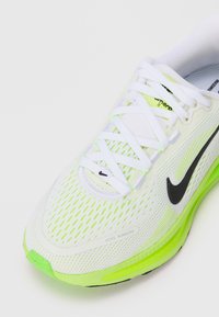 Baskets de course blanches avec un dessus en mesh, accents vert fluo et logo Nike noir. Dotées d'une semelle rembourrée et de lacets blancs.