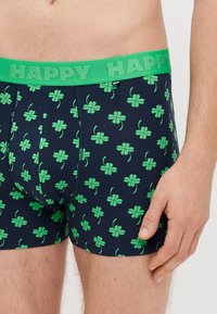 Σκούρα μπλε ανδρικά εσώρουχα τύπου boxer με πράσινο σχέδιο τριφυλλιού και πράσινη ελαστική μέση με την επιγραφή «HAPPY». Κατασκευασμένα από απαλό, ελαστικό ύφασμα για άνεση.
