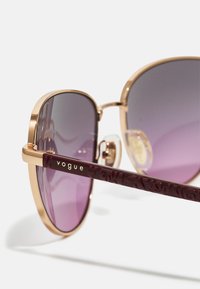 Ochelari de soare cu ramă aurie și lentile gradiate violet. Brațe burgundy cu un model, având brandul "vogue" inscriptionat cu litere aurii.