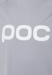 Grå stof med en glat tekstur, der har et fremtrædende hvidt "poc" logo. Designet er simpelt og moderne med rund hals.