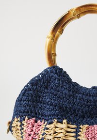 Geflochtener Handtasche mit einem Bambusgriff; besteht aus navy, rosa und beigen Fasern; strukturierte Oberfläche mit einer Mischung aus Häkel- und Webmustern.