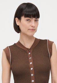 Brązowa, dziana kamizelka bez rękawów z okrągłym kołnierzem, z metalowymi guzikami w kolorze srebrnym z przodu i kontrastowym kremowym obszyciem po bokach.