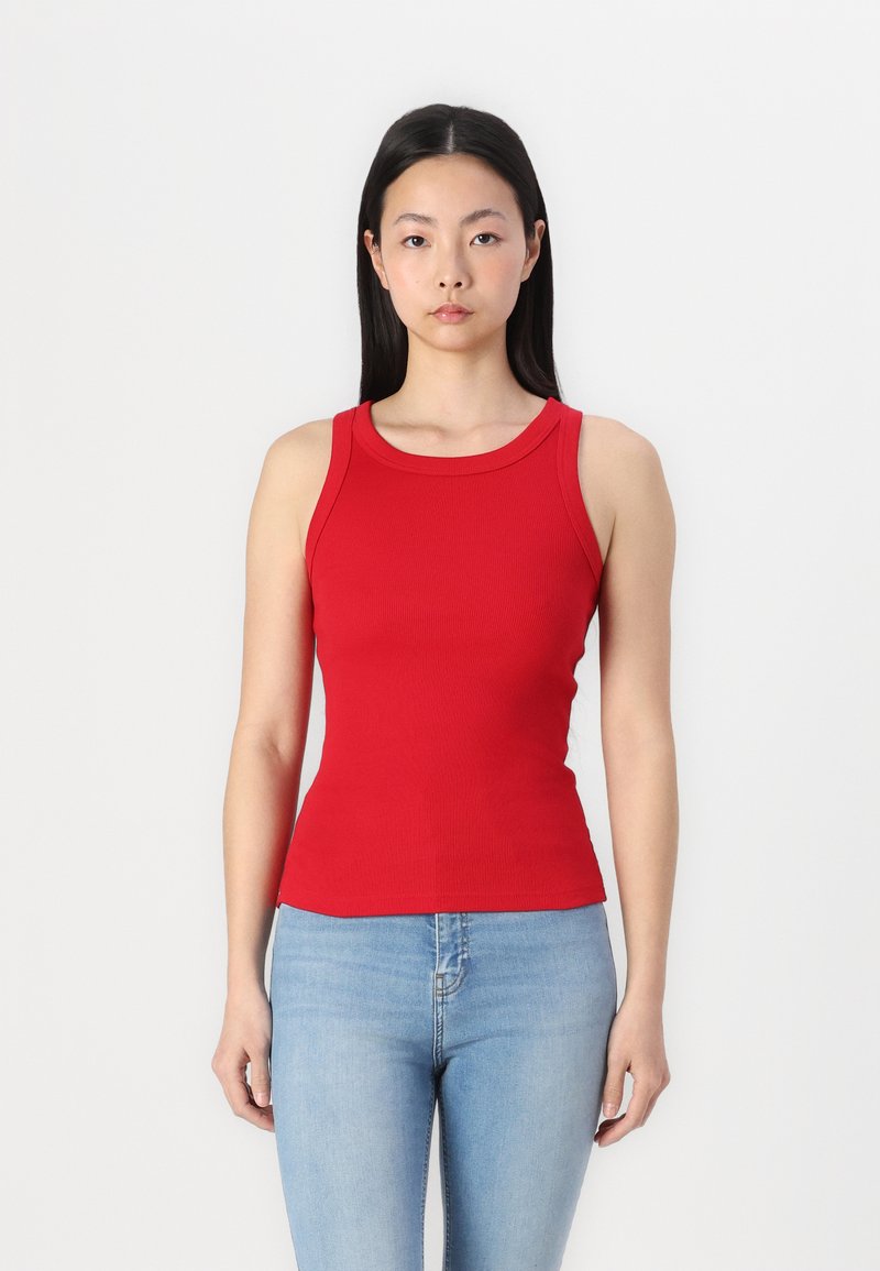 Rød ribbet tanktop med rund halsudskæring og tætsiddende pasform, sammen med lyseblå jeans. Enkel design, ingen synlige mønstre eller accenter.