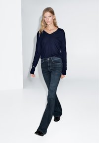 Tmavě modrý černý top s dlouhým rukávem a výstřihem do V v kombinaci s rozšířenými tmavě modrými džíny. Tento outfit má volnější střih a minimalistický design.