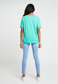 Camiseta de algodón verde menta con un corte relajado, combinada con jeans ajustados de un azul claro y zapatillas blancas. Vista desde la parte posterior.