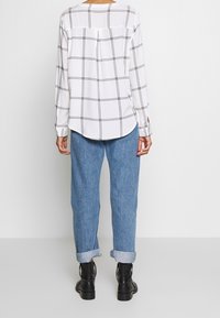 Vit långärmad skjorta med svart rutmönster, matchad med ljusblå jeans med uppvikta ärmar och svarta ankelstövlar.