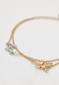 Gold multi-chain bracelet featuring butterfly motifs in rose gold and silver, adorned with clear gemstones and a pearl accent.