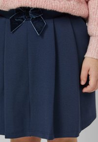 Marineblauer Faltenrock mit einem Samtschleifen-Detail am Bund. Glatte Textur mit sauberem Saumabschluss.
