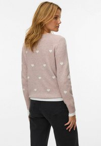 Roze sweater met witte hartpatronen, gemaakt van zacht, gestructureerd fabric. Crew halslijn en geribde manchetten, gecombineerd met donkere broeken.