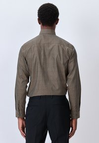 Camicia a maniche lunghe color sabbia con motivo geometrico, con colletto classico e polsini con bottoni. Abbinata a pantaloni neri.