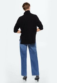 Maglione nero a collo alto, vestibilità ampia con polsini a costine, abbinato a jeans in denim blu a vita alta e gamba dritta e scarpe nere con tacco.