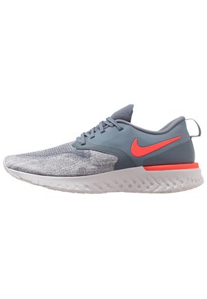 Hellgrauer und blauer Nike Laufschuh mit leuchtend orangefarbenem Swoosh-Logo und weißer, strukturierter Sohle, von der rechten Seite auf weißem Hintergrund dargestellt.