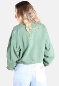 Sweatshirt vert court avec un col rond, un ourlet élastique et une petite étiquette logo sur l'épaule. Tissu doux, coupe décontractée.