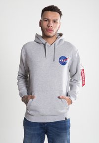 Sivá mikina s kapucňou a logom NASA, predným vreckom, šnúrkami a bočným zipsom s červenou nášivkou. Vyrobená z mäkkej tkaniny s voľným strihom.
