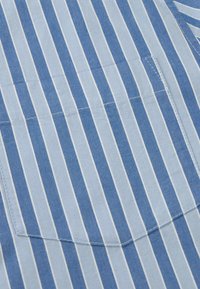 Tissu rayé vertical bleu et bleu clair avec une poche plaquée cousue et de subtiles lignes d'ombre diagonales.