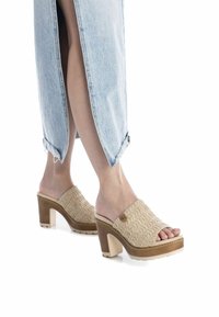 Sandali a zoccolo lavorati a maglia beige con una parte superiore ampia, punta aperta e tacco spesso. Suola leggera con una finitura testurizzata e accenti a contrasto.