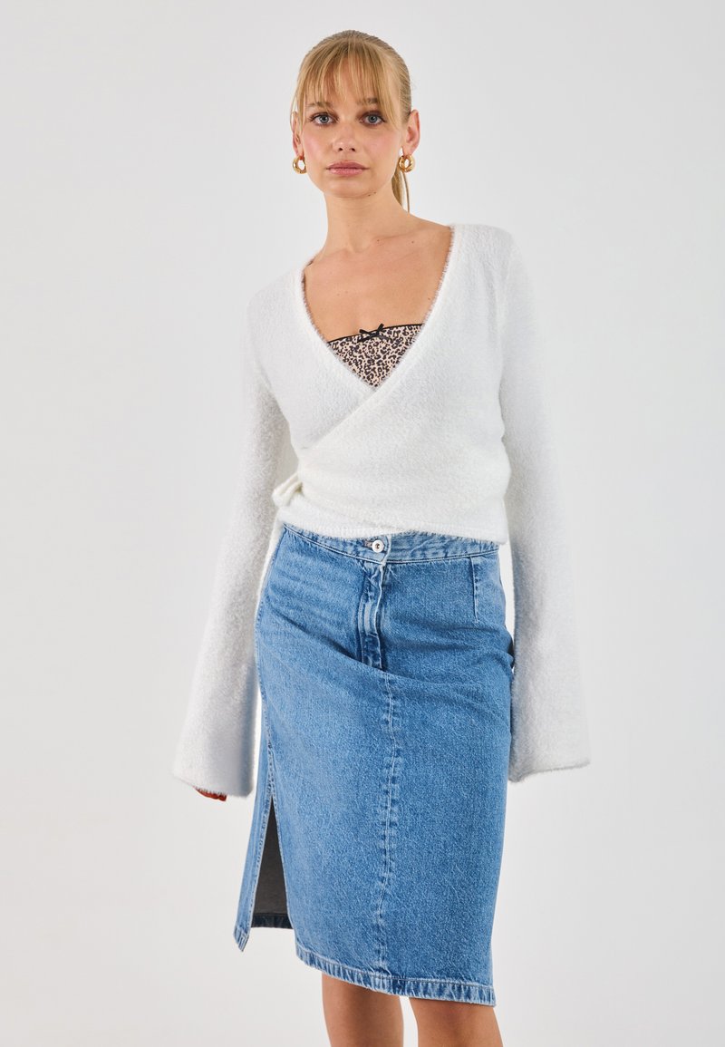 Weißer, flauschiger Wickel-Pullover mit langen Ärmeln über einem schwarz-weißen Leopardenmuster-Oberteil, kombiniert mit einem blauen Jeans-Bleistiftrock mit Seitenschlitz.