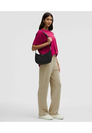 Zwart schoudertasje met een ronde vorm en een gladde textuur; model draagt een magenta t-shirt en beige broek, tegen een effen achtergrond.