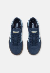 Navy blue suede sneakers with light blue stripes, brown rubber sole, and black laces. Gold branding on the tongue and side accents.