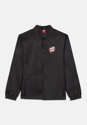 Chaqueta cortavientos negra con cierre de botón, mangas raglán, puños elásticos y un logotipo circular rojo que dice "SANTA CRUZ" en el pecho.