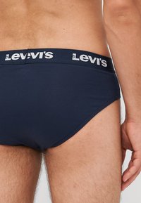 Kék pamut alsónadrág fehér Levi's logóval a derékrészen, szoros szabással és sima textúrával. Látható lábnyílások, minták nélkül.