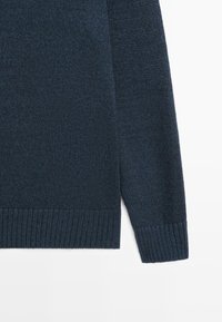Maglione lavorato a maglia in blu navy scuro con polsini e orlo a coste. Tessuto morbido con una vestibilità leggermente ampia, caratterizzato da un taglio dritto.
