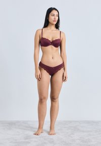 Bordó mežģīņu krūšturis ar mežģīņu apdari un atbilstošas biksītes, ar regulējamām lencēm, gludu apdari un smalkiem bantīšu akcentiem; minimālistisks dizains.