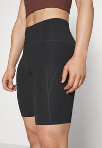 Shorts negros de talle alto hechos de material elástico, con una textura suave, corte ajustado y detalles de costura sutil a lo largo de las costuras.
