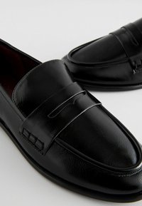 Mustat nahka loaferit, joissa on sileä pinta, leveä nauha jalan päällä ja hienovaraiset ompeluyksityiskohdat reunoilla.
