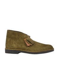 Stivaletto verde in suede con un'etichetta in pelle marrone, punta rotonda, texture morbida e suola in gomma piatta, caratterizzato da un design minimale e dettagli di cucitura.