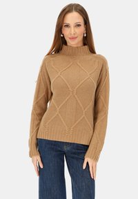 Brązowy dziergany sweter z wysokim kołnierzem i teksturowanym wzorem diamentu. Posiada ściągacze przy rękawach i dole. Połączony z ciemnoniebieskimi szerokimi spodniami jeansowymi.