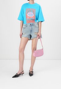 Světle modré oversized tričko s grafickým potiskem, roztrhané denimové šortky a černé lakované lodičky na podpatku. Růžová kabelka s elegantním designem.