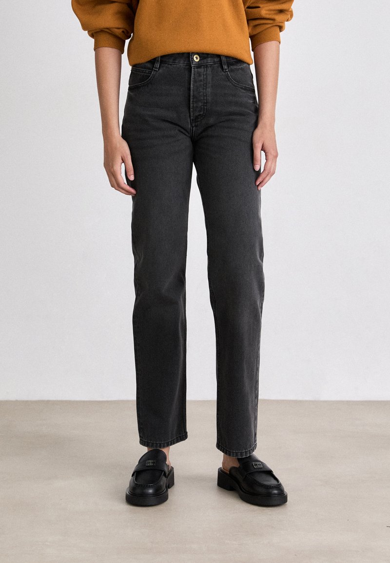 Jeans negros de cintura alta con corte recto. Presentan cinco bolsillos y un cierre frontal con botón. Combinados con mocasines negros de tipo slip-on.