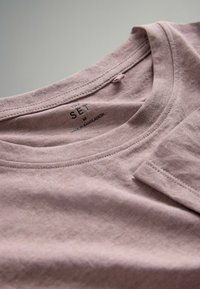 Mėlyna medvilninė marškinė su apvaliu iškirpimu, trumpomis rankovėmis ir matomomis siūlėmis. Etiketėje nurodyta dydis M, pagaminta Bangladeše.