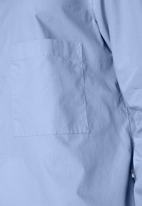 Ljusblå skjorta med en slät yta, featuring en bröstficka och minimala sömnadsdetaljer på sidan.