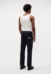 Pantalons en velours côtelé en coton bleu marine, avec une coupe décontractée et une taille élastique. Poche arrière avec détail de marque. Débardeur blanc.
