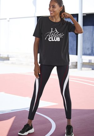 Black athletic T-shirt with white print, paired with black leggings featuring white and red side stripes. Footwear is black sneakers.